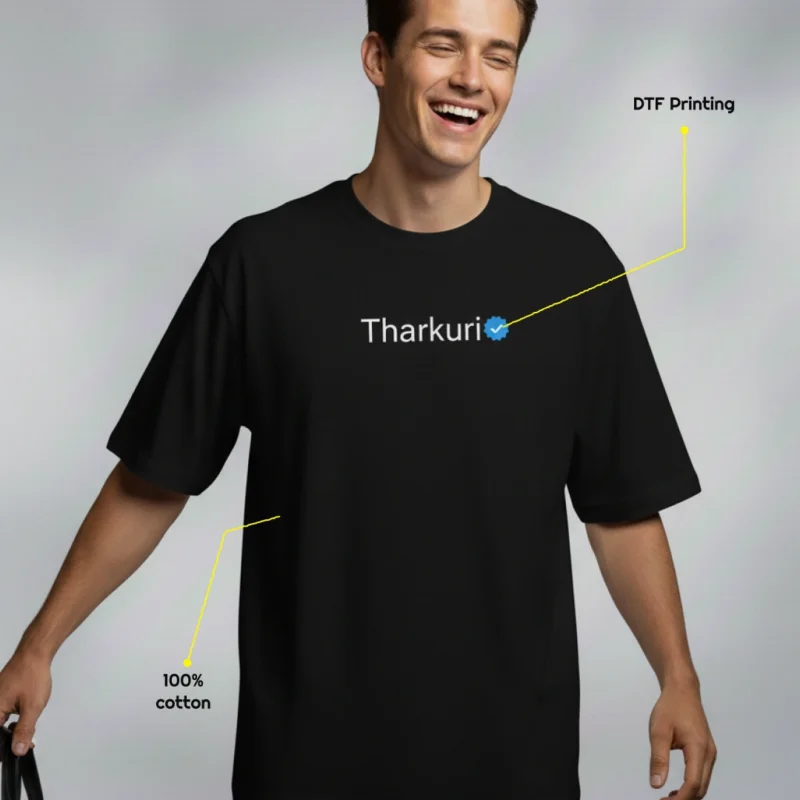 Black oversized 100% cotton “Tharkuri” meme T-shirt with white text and a blue verified-style badge centered on the chest, worn by a model, with small callouts highlighting DTF printing and fabric composition.